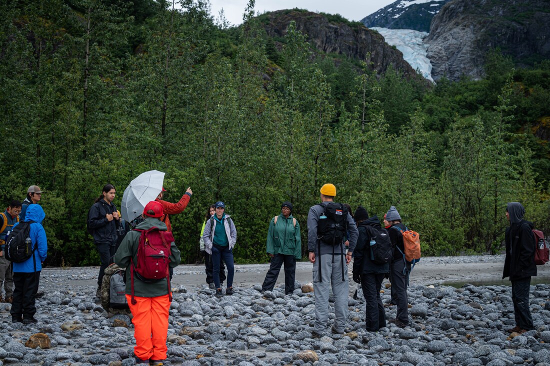 A group of students and faculty standing on a glacial outwash plain discussing science