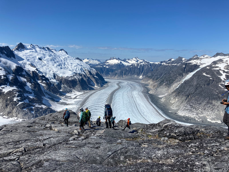 A group of students hiking down a rocky outcrop in front of a glacier
